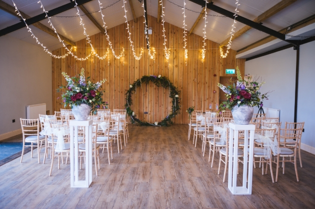 inside of wooden barn set up with ceremony chairs and flower arch at end of aisle