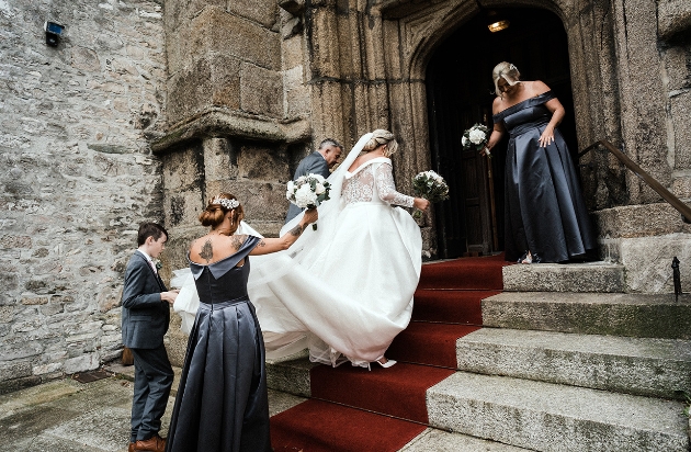Bridesmaids carry bride's train up church steps