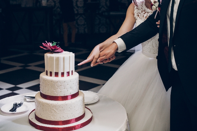 couple cutting a white cake with pink ribbon