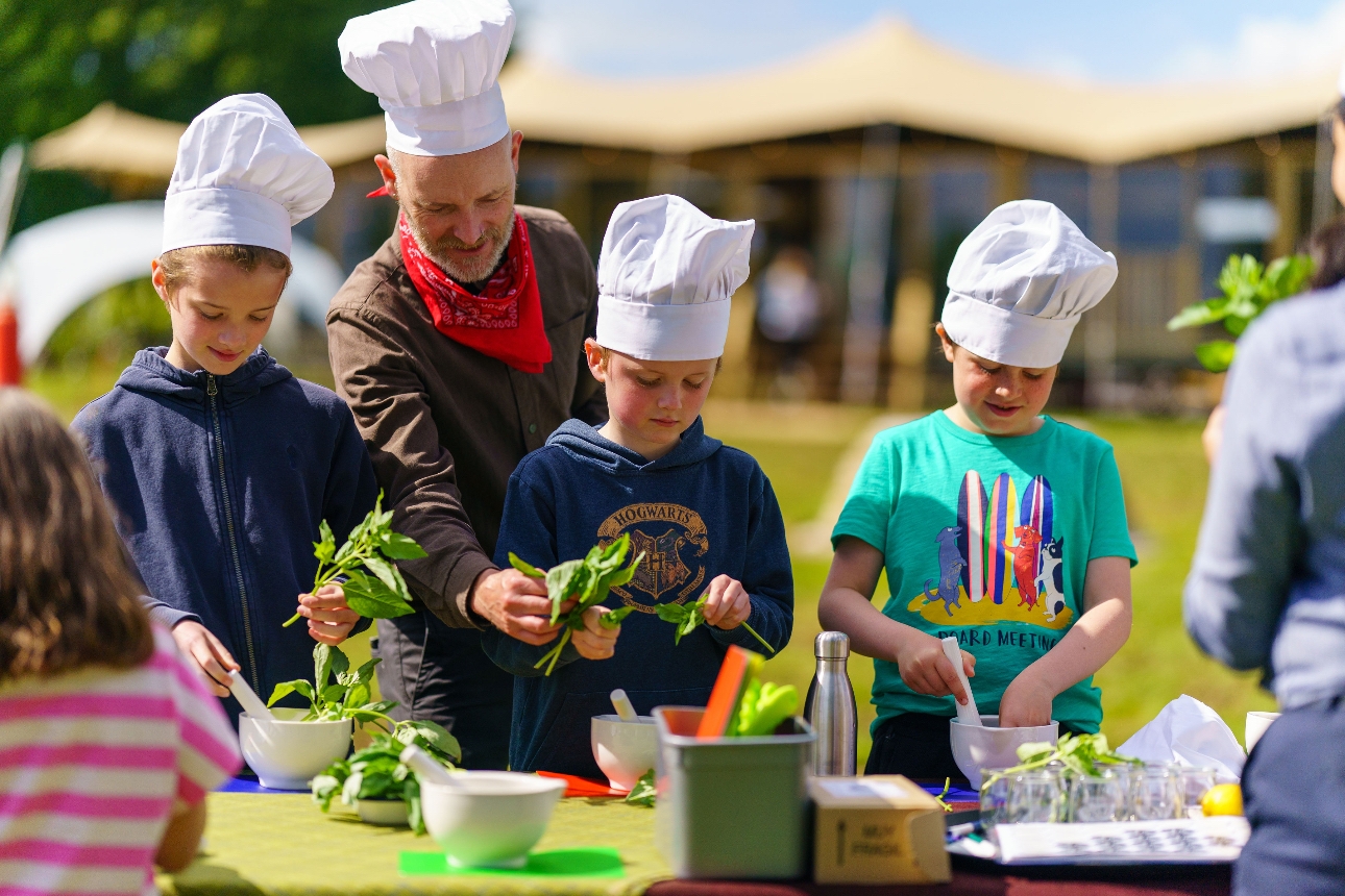 Children wearing chefs hats grind herbs in a pestle and mortar