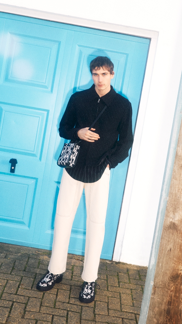 A man standing in front of a blue door dressed in black and white clothes