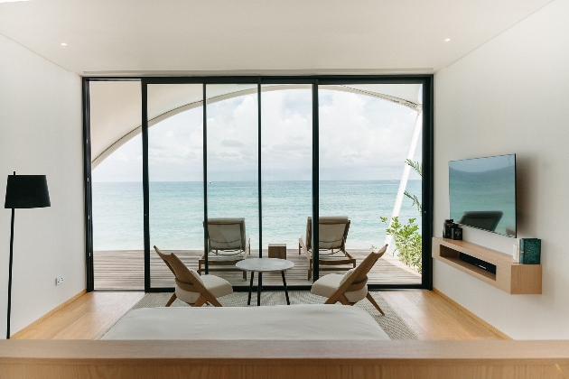 A bedroom with large glass windows overlooking the sea