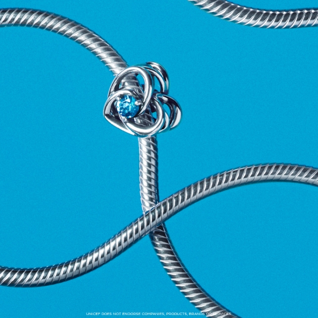 silver chain and charm with blue stone laying on mirrored surface