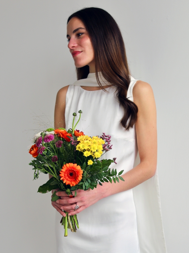 woman posing in sleek wedding dress with a bright bunch of flowers